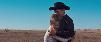 Movie still from “Cimarron” (1960), directed by Charles Walters – A man and a woman hugging each other in a field; Medium shot, Low angle