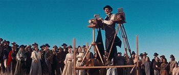 Movie still from “Cimarron” (1960), directed by Charles Walters – An old fashioned man standing on top of an old fashioned camera; Wide shot, Low angle