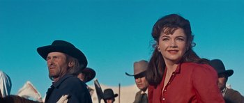 Movie still from “Cimarron” (1960), directed by Charles Walters – A woman in a red shirt is standing in front of a group of men; Medium shot, Low angle