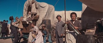Movie still from “Cimarron” (1960), directed by Charles Walters – A group of people standing next to each other near a covered wagon; Wide shot, Low angle