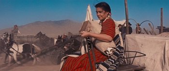 Movie still from “Cimarron” (1960), directed by Charles Walters – A woman sitting on a chair in the desert; Medium shot, Low angle
