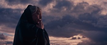 Movie still from “Cimarron” (1960), directed by Charles Walters – An older woman standing in front of a cloudy sky; Close Up shot, Low angle