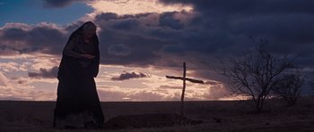 Movie still from “Cimarron” (1960), directed by Charles Walters – A person standing in front of a cross on a cloudy day; Wide shot, Low angle