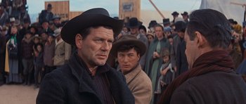Movie still from “Cimarron” (1960), directed by Charles Walters – A man in a crowd of people wearing a hat; Medium shot, Over the shoulder angle
