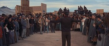 Movie still from “Cimarron” (1960), directed by Charles Walters – A crowd of people standing around a man in front of a building; Wide shot, Low angle