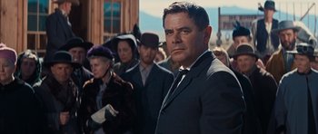 Movie still from “Cimarron” (1960), directed by Charles Walters – A man in a suit and tie standing in front of a group of people; Medium shot, Over the shoulder angle