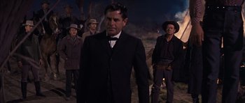 Movie still from “Cimarron” (1960), directed by Charles Walters – A man in a suit and tie standing in front of a group of men; Medium shot, Low angle