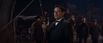Movie still from “Cimarron” (1960), directed by Charles Walters – A man in a suit holding a rifle in front of other men; Medium shot, Low angle