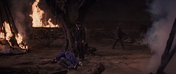 Movie still from “Cimarron” (1960), directed by Charles Walters – A man in a suit standing next to a corpse; Wide shot, High angle