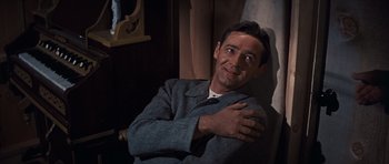 Movie still from “Cimarron” (1960), directed by Charles Walters – A man sitting in a chair with his arms folded on his chest; Close Up shot, Low angle