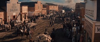 Movie still from “Cimarron” (1960), directed by Charles Walters – A group of people walking on a dirt road near buildings; Extreme Wide shot, High angle