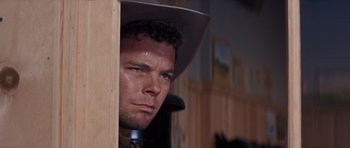 Movie still from “Cimarron” (1960), directed by Charles Walters – A man in a cowboy hat looking out of a window; Close Up shot, Low angle