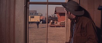 Movie still from “Cimarron” (1960), directed by Charles Walters – A man standing in front of an open window looking out at a train yard; Wide shot, Over the shoulder angle