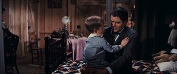 Movie still from “Cimarron” (1960), directed by Charles Walters – A man in a suit holding a young boy; Medium shot, Over the shoulder angle
