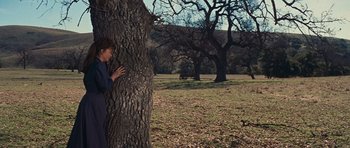 Movie still from “Cimarron” (1960), directed by Charles Walters – A woman leaning against a tree in a field; Wide shot, Over the shoulder angle