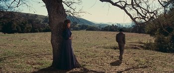 Movie still from “Cimarron” (1960), directed by Charles Walters – A woman standing next to a tree in a field; Wide shot, Low angle