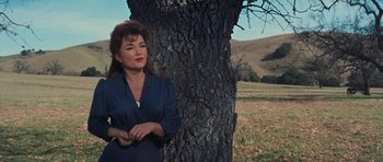Movie still from “Cimarron” (1960), directed by Charles Walters – A woman standing next to a tree in a field; Medium shot, Low angle
