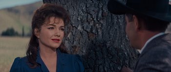 Movie still from “Cimarron” (1960), directed by Charles Walters – A woman standing in front of a tree trunk; Close Up shot, Over the shoulder angle