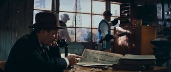 Movie still from “Cimarron” (1960), directed by Charles Walters – A man in a hat is reading a newspaper; Medium shot, Over the shoulder angle
