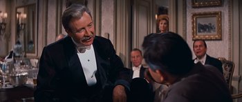 Movie still from “Cimarron” (1960), directed by Charles Walters – An older man in a tuxedo talking to a younger man in a suit; Medium shot, Over the shoulder angle