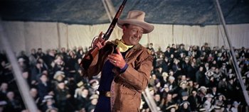 Movie still from “Circus World” (1964), directed by Henry Hathaway – A man holding a rifle in front of an audience; Medium shot, Low angle