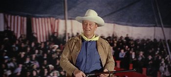 Movie still from “Circus World” (1964), directed by Henry Hathaway – A man in a cowboy hat holding a rifle; Medium shot, Low angle