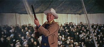 Movie still from “Circus World” (1964), directed by Henry Hathaway – A man holding a rifle in front of an audience; Medium shot, Low angle