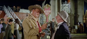 Movie still from “Circus World” (1964), directed by Henry Hathaway – A man in a trench coat and a cowboy hat talking to another man in a suit; Medium shot, Over the shoulder angle
