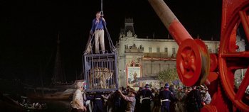 Movie still from “Circus World” (1964), directed by Henry Hathaway – A man standing on top of a cage in front of a crowd of onlookers; Wide shot, Low angle