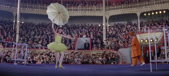 Movie still from “Circus World” (1964), directed by Henry Hathaway – A woman in a yellow dress holding an open umbrella; Wide shot, Low angle