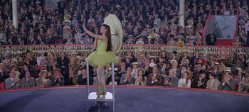 Movie still from “Circus World” (1964), directed by Henry Hathaway – A woman in a yellow dress holding an umbrella; Wide shot, High angle