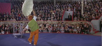 Movie still from “Circus World” (1964), directed by Henry Hathaway – A man standing in front of an audience holding a flag; Wide shot, Low angle