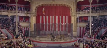 Movie still from “Circus World” (1964), directed by Henry Hathaway – A man is jumping over a bunch of animals in a cage; Extreme Wide shot, High angle