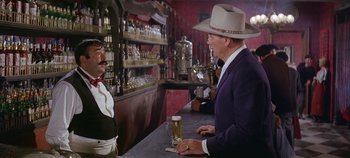 Movie still from “Circus World” (1964), directed by Henry Hathaway – A man in a cowboy hat is standing at a bar talking to another man; Medium shot, Over the shoulder angle