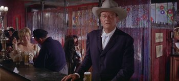 Movie still from “Circus World” (1964), directed by Henry Hathaway – A man in a suit and a cowboy hat is standing at a bar with a beer; Medium shot, Low angle