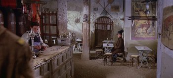 Movie still from “Circus World” (1964), directed by Henry Hathaway – A man sitting at a table in a room; Wide shot, High angle