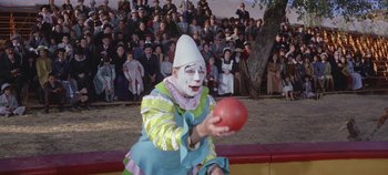 Movie still from “Circus World” (1964), directed by Henry Hathaway – A clown holding a ball in front of a crowd of people; Wide shot, High angle