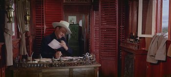 Movie still from “Circus World” (1964), directed by Henry Hathaway – A man wearing a cowboy hat is sitting at a desk; Medium shot, High angle