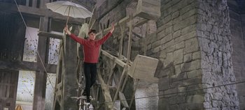 Movie still from “Circus World” (1964), directed by Henry Hathaway – A man holding an umbrella while standing on top of a ladder; Wide shot, Low angle