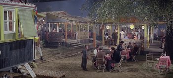 Movie still from “Circus World” (1964), directed by Henry Hathaway – A group of people sitting at a table outside; Extreme Wide shot, High angle