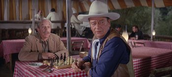 Movie still from “Circus World” (1964), directed by Henry Hathaway – A man wearing a cowboy hat playing a game of chess; Medium shot, Over the shoulder angle