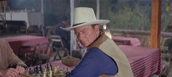 Movie still from “Circus World” (1964), directed by Henry Hathaway – An older man wearing a cowboy hat playing a game of chess; Medium shot, Over the shoulder angle