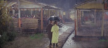 Movie still from “Circus World” (1964), directed by Henry Hathaway – A man and a woman walking under an umbrella in the rain; Wide shot, High angle