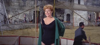 Movie still from “Circus World” (1964), directed by Henry Hathaway – A woman in a black bathing suit and a green jacket; Medium shot, Low angle