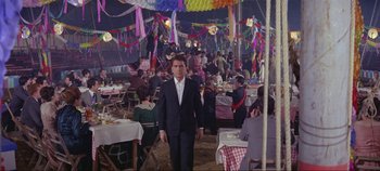 Movie still from “Circus World” (1964), directed by Henry Hathaway – A man in a suit standing in front of a crowd of diners; Wide shot, High angle