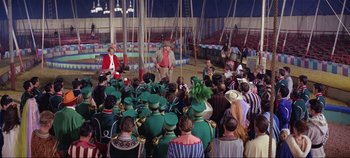 Movie still from “Circus World” (1964), directed by Henry Hathaway – A group of people sitting in a circle on a field at night; Wide shot, High angle