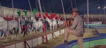 Movie still from “Circus World” (1964), directed by Henry Hathaway – A man sitting in front of a group of white horses; Wide shot, Low angle
