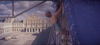 Movie still from “Circus World” (1964), directed by Henry Hathaway – A woman hanging from ropes on the side of a building; Wide shot, Low angle