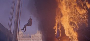Movie still from “Circus World” (1964), directed by Henry Hathaway – A man hanging from a rope while a fire rages in the background; Wide shot, Low angle