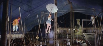 Movie still from “Circus World” (1964), directed by Henry Hathaway – A woman in a blue dress holding an open umbrella; Wide shot, Low angle